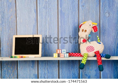 Stuffed animal Giraffe sitting against blue wooden background with other toys at home