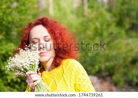 close up red haired dreamy girl with closed eyes posing with bouquet of white flowers in yellow sweater