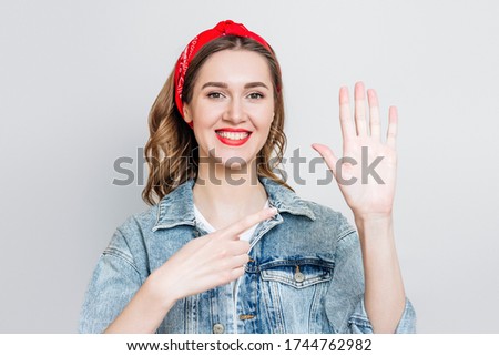 Student girl in denim jacket, bandana smiles and points to her left hand isolated on gray background, left-handed woman celebrating left-handed day Royalty-Free Stock Photo #1744762982
