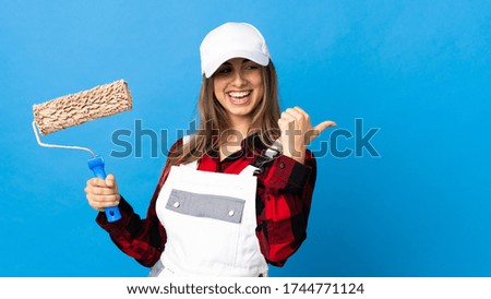 Painter woman over isolated blue background pointing to the side to present a product