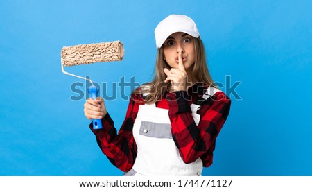 Painter woman over isolated blue background showing a sign of silence gesture putting finger in mouth