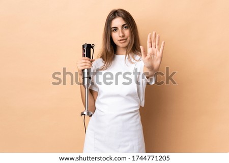 Woman using hand blender over isolated background making stop gesture