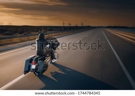 
A motorcycle driver rides alone on an asphalt highway. Biker in motion on an empty road during sunset Royalty-Free Stock Photo #1744784345