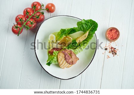 Caesar salad with croutons, parmesan, bacon, chicken, egg in white bowl on white background. Restaurant serving. Close up with copy space.