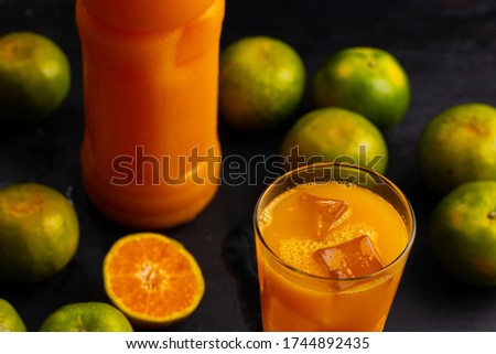 Picture of fresh orange juice in a bottle and in a glass. They are place among fresh green orange. The orange juice in glass is also filled with ice