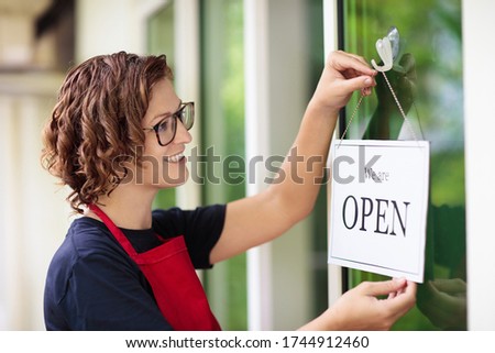 Cafe opening after lockdown. Open sign on front door of restaurant or grocery store. Waiter in apron greeting customer. Welcome message on bakery entrance. Back to work after quarantine.