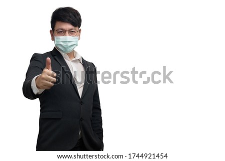 Asian businessman wearing surgical face mask in formal black suit jacket, show trumps up by right hand, look at the camera, studio light isolated on white background, concept for coronavirus, covid19