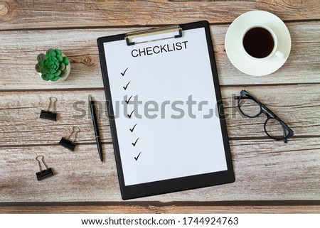 Checklist on blank page with pen, green plant, cup of coffee, eyeglasses and paper clips top view on wooden office or home table