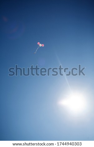 blue sky with bright sun against which flies three balloons