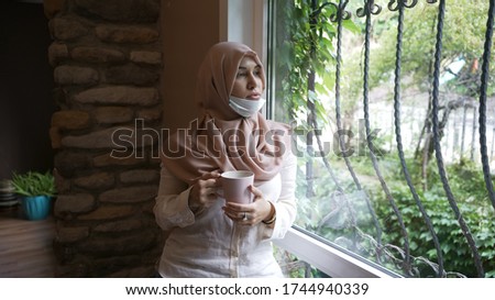 Young muslim woman in office, drinking coffee wearing a mask.