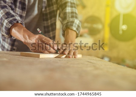 Carpenter working on woodworking machines in carpentry shop. Asian craftsman works in a workplace. Cabinet maker at the table with pencil drawing sign on plank