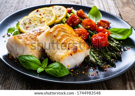 Fish dish - fried cod fillet with asparagus on wooden table 