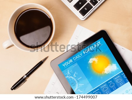 Workplace with tablet pc showing weather forecast and a cup of coffee on a wooden work table close-up