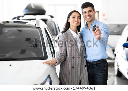 New Car Owners. Young Famile Standing In Dealership Store, Man Showing New Car Key, Free Space