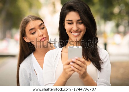 Jealous Friend. Envious Girl Peeking At Girlfriend's Phone While She Texting Walking Together Outdoors Royalty-Free Stock Photo #1744996787