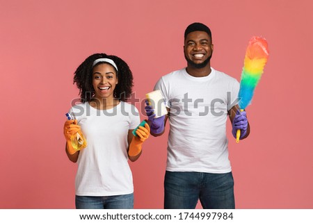 Ready For Housework. Positive Black Couple Posing With Cleaning Tools In Hands On Pink Studio Background, Holding Sponges, Sprayer And Duster