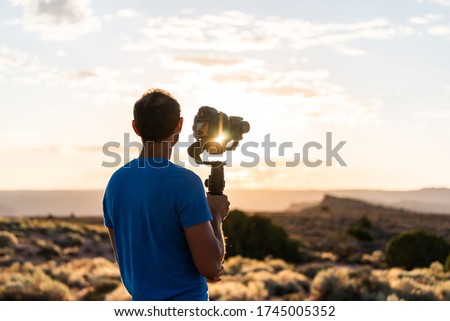 Man holding gimbal camera stabilizer filming sunrise with sunburst flare through equipment in Arches National Park, Utah at Fiery Furnace Viewpoint