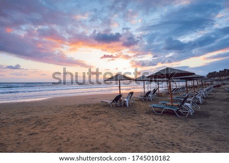 Empty beach with umbrellas and deck chairs closed. Unbelievable sunrise. 2020 summer quarantine travel. Beautiful summertime view seascape. Relax places island Crete, Greece.