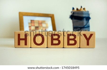 Wooden cubes with the inscription 'hobby'. Frame with a picture and a bag with pencils in the background. Beautiful white background, copy space.