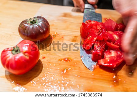 Man chopping vegetables on cutting board table in kitchen picking up juicy red and black heirloom tomatoes with vibrant color from garden Royalty-Free Stock Photo #1745083574