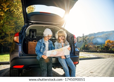 Agreeable boy and girl are looking at the road map while sitting in the auto's trunk and discussing the move direction. Family vacation trip by car. Royalty-Free Stock Photo #1745090051