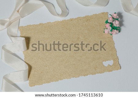 Blank wedding invitation next to a ribbon and small pink flowers on a white background