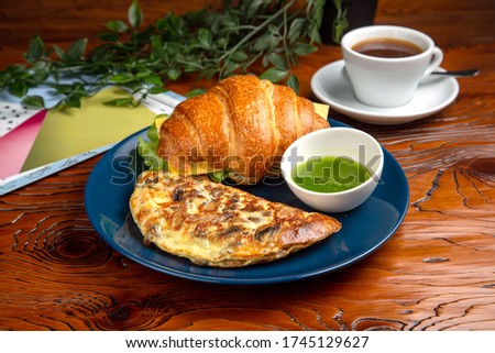 Egg omelet, fresh croissant, pesto sauce, black coffee. Breakfast is on the table.