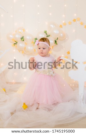 Cute little girl in a pink princess dress with a flower on her hair plays with wooden ballerinas among the golden stars on the background of a large white wooden moon and balloons. Children's decor. 