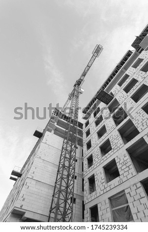 Black and white photo of a multi-storey residential building under construction and crane on a background of blue sky