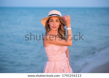 
Young girl on vacation by the sea. Sunset at sea. Happy young woman in a dress and with a hat walks on the coast. Family context. Travel and Relax