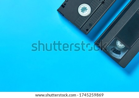 Two black old plastic vhs video cassettes lies on blue desk. Concept of 90s. Copy space. Flat lay