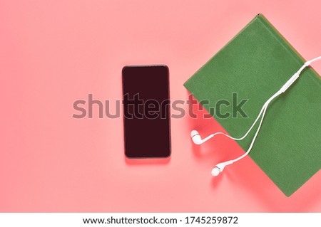 Smartphone or tablet with headphone and green old book on pink background. Audiobook concept. Online education. E-learning. Modern technology