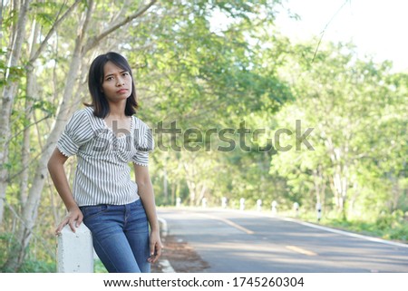 Asian woman waiting for a bus on the side of the road