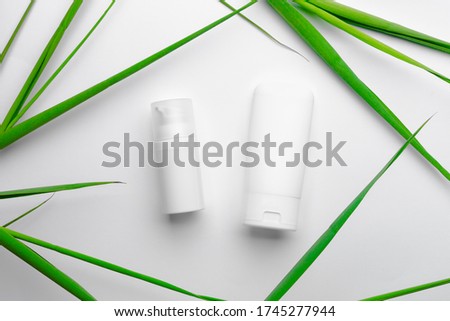 White tubes with face and body cream on white background with green leaves. Special face treatment for summer.