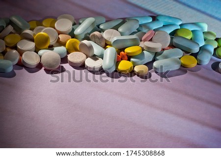 White, yellow, red, orange and blue pills on a purple cardboard background. Medication on a dark background with contrasting dramatic light.