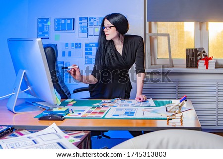 Design applications.  Designer is working on the layout of the mobile application. Woman in web design studio. Girl with a marker looks into the monitor. UX design. Mobile site development. 