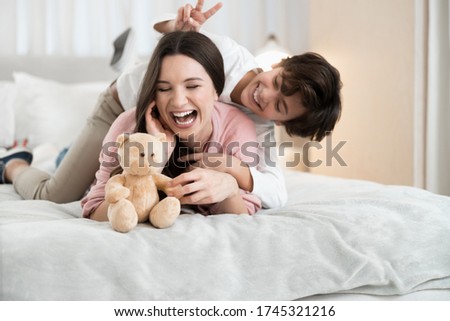 Front view of a mischievous cute Caucasian boy making rabbit ears behind his mother head