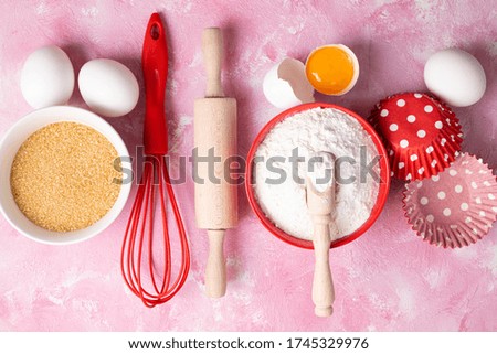 Baking background. Ingredients for baking cakes or muffins. Kitchen utensils, flour, eggs on pink table. Flat lay, top view
