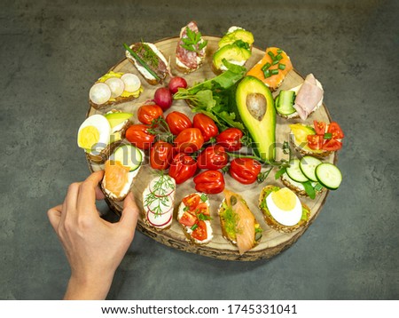 a large wooden tray with butterbreads and a hand takes one of them on a gray wooden background