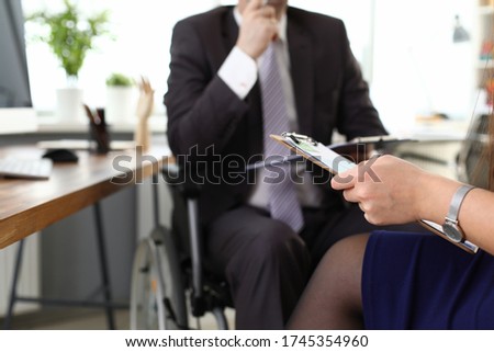 Male boss on wheelchair speaks with woman in office. Prestigious job for people with disabilities. Man in suit sits in wheelchair. Protection labor rights workers with disabilities Royalty-Free Stock Photo #1745354960