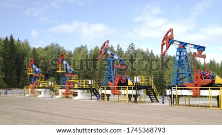 Industrial oil well pump jacks pumping crude oil for fossil fuel energy with drilling rigs in oil field. Nodding donkey pumps working in middle of forest in sunny summer day. Oil mining machines.