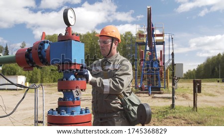 Oilman in orange helmet and protective glass closing valve of x-mass wellhead to shut off well. Decline in oil production after adoption of agreements at meeting of OPEC to stabilize price of oil.