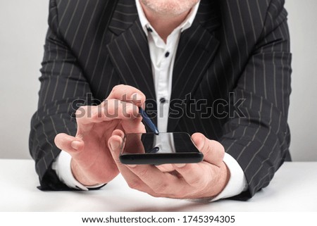 Businessman shows screen of a smartphone. Man in a suit shows phone. Concept - man shows  image on screen. Stylus and smartphone in hands of a businessman. Investor app. Demonstration application
