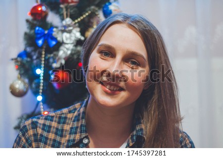 girl in a checkered shirt sitting near the Christmas tree