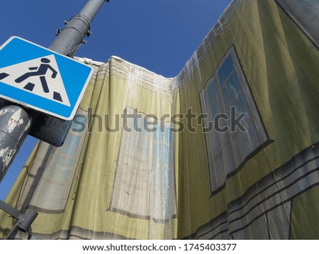 Corner of a building closed by fabricwith a printed windows and a pedestrian crossing sign.