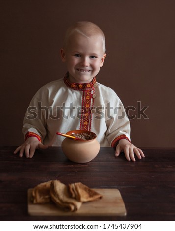 Russian folk style. a boy in a Russian folk shirt. tradition of Russia. Carnival costume. Russian festivities. porridge in a clay pot. Bogatyr. peasant. Maslenitsa. holiday. Maslenitsa collection Royalty-Free Stock Photo #1745437904