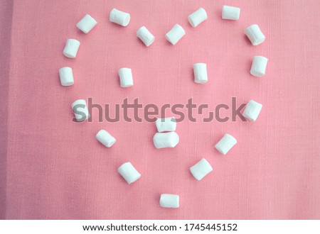 Small marshmallows laid out in the shape of a heart on a soft pink linen background