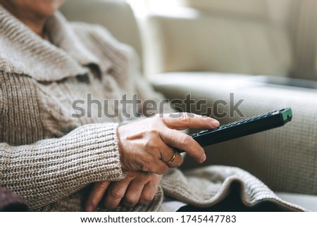 Asian elderly hand holding remote television. Senior people relax from work wear sweater sit on sofa watching tv movie in living room stay at home. Royalty-Free Stock Photo #1745447783