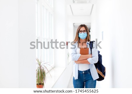Student in protective face mask in empty college indoors. Young woman going to exams in high school. Girl with backpack and book in university corridor during quarantine, lockdown.