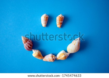 Happy emoji made of seashells on blue background. Summer, fun, vacation, travel, journey concept.